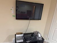 Photo of the TV mounted on wall with remote and accessories on a table beneath