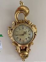 Front view of vintage gilded plaster wall clock showing ornate frame and clock face with Roman numerals.