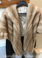 Mink stole hanging on a black hanger, showing fur texture and satin interior lining.