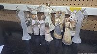 Front view of 12 angel figurines including clear acrylic, Willow Tree style, and Elements brand figures, various sizes and poses