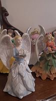 Photo showing four Avon Four Seasons angels from 2006, each dressed in seasonal-themed gowns with floral accessories, detailed silver wings.