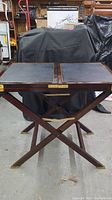 Front view of the bar table with folded leaves, showing the leather-like top and brass accents, with an X-frame wooden base.