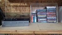 Photo of LG Blu-ray player, Magnavox VHS/DVD player, and plastic container filled with DVD cases on wooden surface.