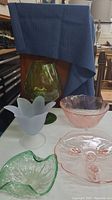 Group photo of green glass vase, frosted tulip dish, green leaf dish, pink bowl, and pink footed plate with floral etching on white table.