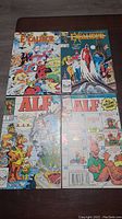 Four comic books including two Excalibur and two ALF comics laid out on table