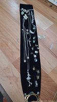 Full lot laid out on black fabric showing necklaces, brooches, earrings, and pendants spread out on hardwood floor.
