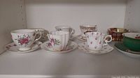 Wide view of all 8 cups and saucers arranged in a single shelf, showing variety of floral designs and colors