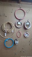 Photo showing a variety of embroidery hoops in plastic and wood, including pink, blue, white, and natural wood colors of various sizes hanging on pegboard