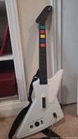 Full view of Guitar Hero guitar controller with white Gibson Explorer-style body, black neck and colored fret buttons.