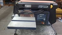 Front and top view of the Mastercraft tabletop belt sander showing the sanding belt, work table, and power cord wrapped around the tool.