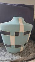 Front angle showing the flat wide shoulder and the turquoise matte surface with black and white geometric shapes.