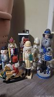 Seven assorted nutcrackers standing grouped on floor including lady with dog, baseball player, soldier types, and rocking horse rider.