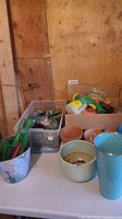 Photo of various planters (ceramic, plastic), gardening tools with green handles, and Miracle-Gro sprayer bottles on a table.