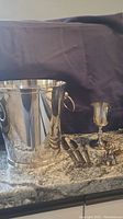 Photo of the silver-plated ice bucket, goblet, utensils, and candle snuffer displayed on a granite countertop against a dark background.