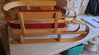 Side view of wooden kids sled showing red seat and side rail accents, curved runners, and attached yellow pull rope.