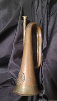 Full side view of the bugle showing its curved shape, patina, and decorative emblem on bell.