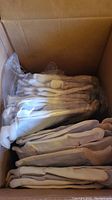Box with stacked pairs of white cloth work gloves wrapped in plastic and loose gloves.