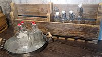 Handcrafted oak pallet rack shown holding clear glass sealable bottles with one galvanized tray in front