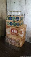 Two 12-count boxes of assorted 1 litre canning jars and two 12-count boxes of jelly jars, stacked with some jars displayed out of the boxes