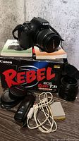 Canon EOS Rebel T3i camera body with lenses, remote trigger, battery, charger, USB cable, original box and manuals shown sitting on surface.