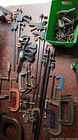 Overview of all clamps laid out on floor, showing variety including pipe clamps, bar clamps, C clamps, and spring clamps in box