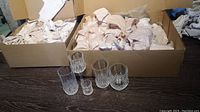Photo of five different styles of clear cut crystal glasses placed in front of two open boxes with packing paper inside.