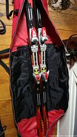 Pair of adult downhill skis inside a red and black ski bag, showing bindings.