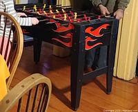 Black foosball table with red and yellow players on rods, decorated with flame patterns on sides