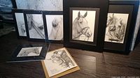 Seven horse art pieces arranged on floor, showing framed and matted prints with detailed pencil drawings of horses.