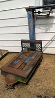 Side angled view of vintage heavy platform scale showing wooden plank surface and metal frame with rust and chipped blue paint.