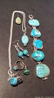 Full set arranged on black surface showing all jewelry including necklace, earrings, two rings, and bracelet with multiple turquoise stones.