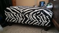 Side view of zebra print storage bench showing hinged top and bun feet, with visible chip on one foot.