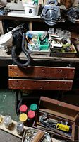 Overview of lot showing wooden folding workbench, DirtVac vacuum cleaner with hose, worklamp, wooden toolbox, and assorted hardware in boxes.