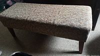 Photo of the full bench showing the fabric upholstery on the rectangular seat and the four wood legs.