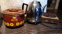 Overall view of all three items together: General Electric percolator, Sunbeam Mini-Crock slow cooker, and electric warming plate on wooden base.