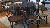 Four Windsor style wood chairs, one armchair with arms, three side chairs, showing wear and aging.
