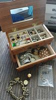Wooden jewellery box open to show earrings, rings and brooches inside compartments.
