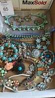 Top-down view of assorted bracelets, brooches and earrings with turquoise beads, floral designs, and metallic elements in a box, showing varied textures and colors.