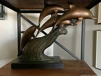 Full view of the brass dolphin sculpture showing four dolphins leaping over a wave base on a wooden surface.