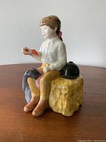 Front side view of Royal Doulton First Prize figurine showing seated child holding red ribbon on yellow haystack.