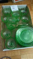 Box containing eleven green glass footed fruit nappies and eleven matching side plates stacked together.