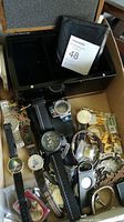 Photo showing multiple wristwatches with various straps and faces, cufflinks, jeweller's loupe, vintage pen set, Harley Davidson belt buckle, and leather bracelet in a black dresser box.