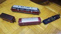 Four Fleischmann model train parts including a red diesel locomotive body, passenger car body, brown freight car, and chassis with motor.