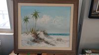 Framed acrylic painting depicting a beach landscape with palm trees, dunes, seagulls, and ocean under a blue sky, hung on wall near window