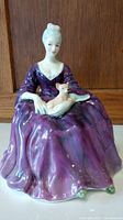 Front view of Royal Doulton Charlette figurine showing woman in purple dress holding small dog.