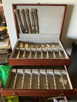 Full view of the wooden canteen case open showing multiple tiers of silver-plated flatware for 12 people.