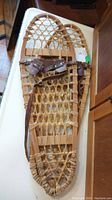 Pair of vintage wooden framed snowshoes with rawhide webbing lying flat, showing overall shape and condition.