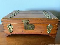 Closed wooden box showing finger joint corners, brass lock, and decorative brass strips on lid.