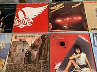 Top view showing front covers of 9 vinyl record albums, identifiable titles include Aerosmith, Bob Marley & The Wailers 'Rastaman Vibration', Pointer Sisters, Black Sabbath, Sheena Easton, The Doors and The Rolling Stones live album.