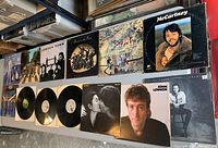 13 Beatles and solo artist vinyl record covers arranged on table, showing titles and artwork including Abbey Road and solo albums by John Lennon and Paul McCartney.